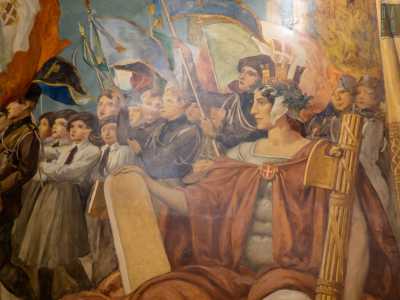 Le due organizzazioni giovanili istituite da Mussolini sfilano davanti a una laureata in primo piano che posa sui ragazzi lo sguardo austero e regge tra le braccia un fascio littorio